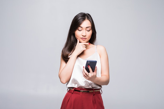 白い壁に分離されたスマートフォンを使用して若いアジア女性。