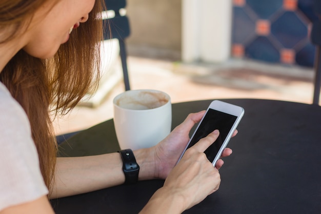 スマートフォンを使用している若いアジア人の女性は、カフェで空白の黒い画面をモックアップ