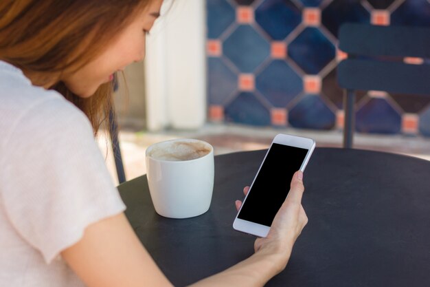 スマートフォンを使用している若いアジア人の女性は、カフェで空白の黒い画面をモックアップ