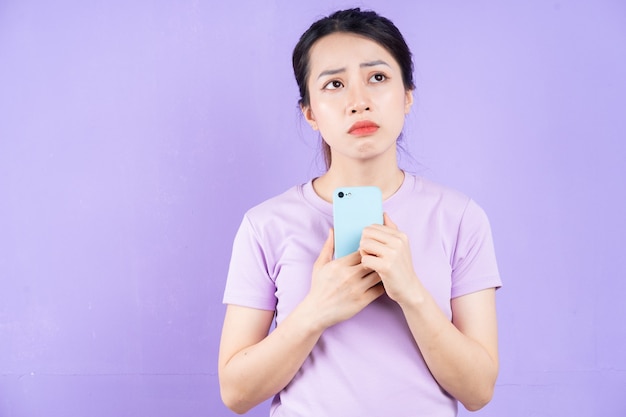 Молодая азиатская женщина с помощью смартфона на фиолетовом фоне