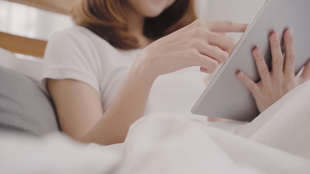 Young Asian woman using tablet while lying on bed after wake up in the morning