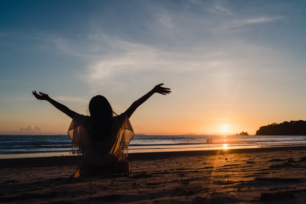 ビーチの近くの夕日を見ている若いアジア女性、幸せなリラックスした夜の夕日時をお楽しみください。