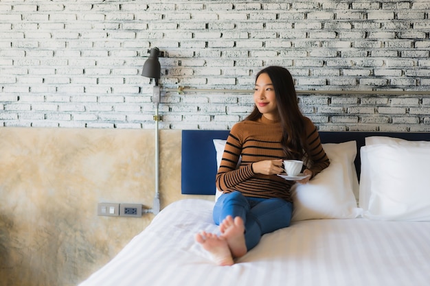 Giovane donna asiatica con la tazza di caffè sul letto