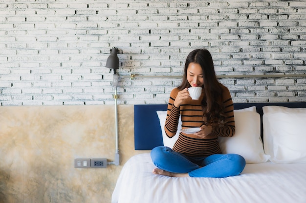 ベッドの上のコーヒーカップを持つ若いアジア女性