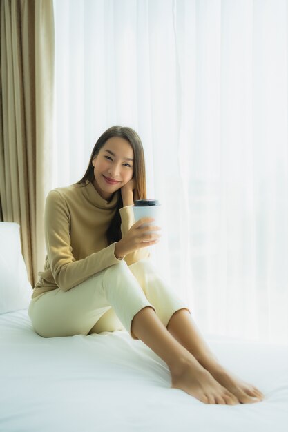침대에 커피 컵과 젊은 아시아 여성