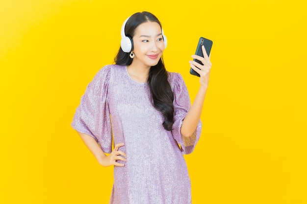 黄色で音楽を聴くためのヘッドフォンとスマートフォンを持つ若いアジアの女性