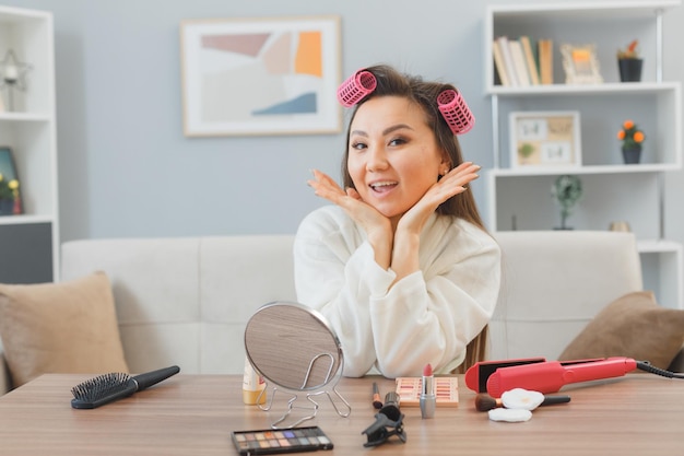 긴 검은 머리를 한 젊은 아시아 여성, 집에서 화장대에 헤어 컬러링을 하고 아침 화장을 하며 행복하고 긍정적인 미소를 짓고 있습니다.