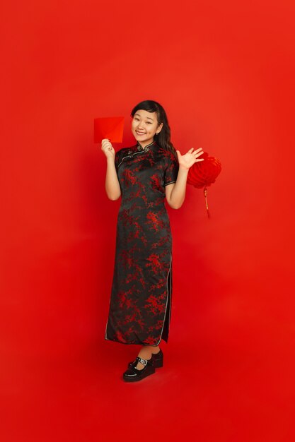Молодая азиатская женщина с красным конвертом и китайским фонарем, изолированным на красной стене