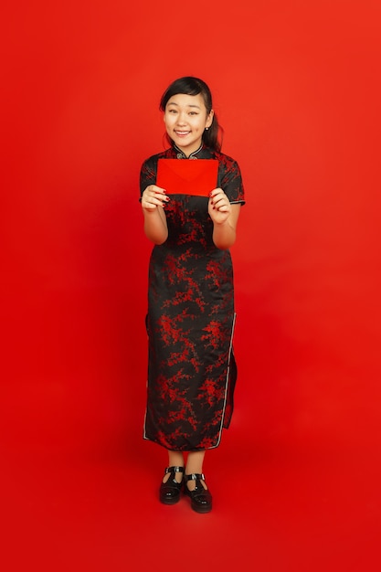 Молодая азиатская женщина с красным конвертом, изолированным на красной стене