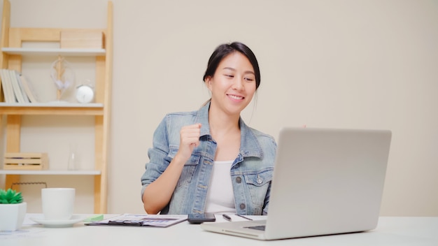 Young asian woman working using laptop on desk in living room at home. asia business woman success celebration feeling happy dancing at home office.