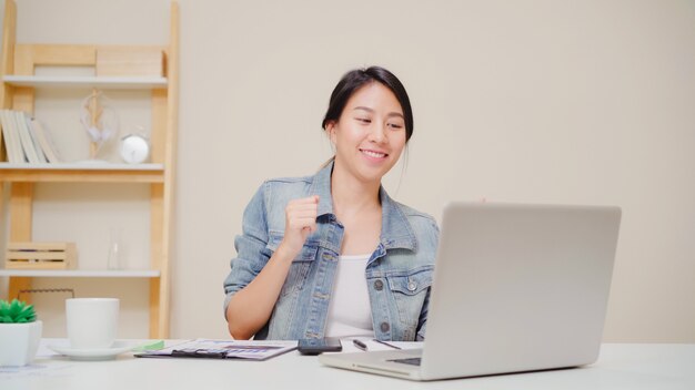Young asian woman working using laptop on desk in living room at home. Asia business woman success celebration feeling happy dancing at home office.