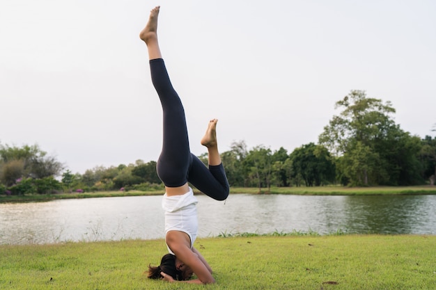 Молодая азиатская йога женщины outdoors держит спокойствие и размышляет пока практикующ йогу