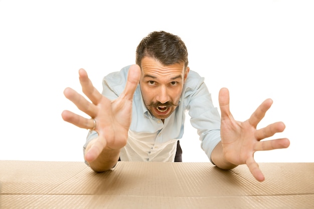 Young astonished man opening the biggest postal package isolated on white. Shocked male model on top of cardboard box looking inside. 