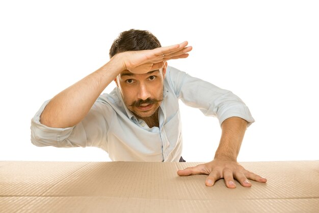 Young astonished man opening the biggest postal package isolated on white wall