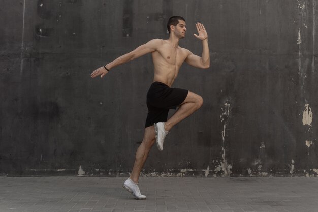 Молодой спортсмен человек, голый торс, бежит к серой стене
