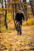 Free photo young athlete man riding sports bike on track in autumn park