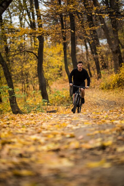 Молодой спортсмен ездить с велосипедом на Осенний парк. Подготовка к тренировке