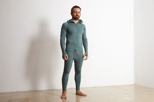 Young athlete wers green merino wool baselayer thermal suite in winter time, posing in front of white wall