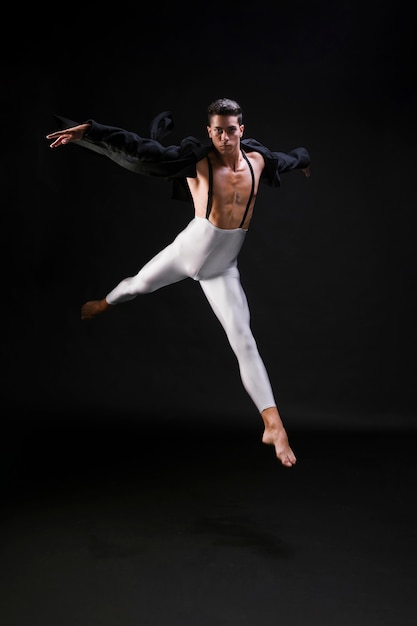 Young athletic male jumping and dancing on black background