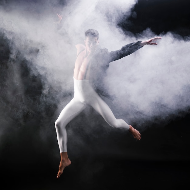 Free photo young athletic man jumping and dancing near smoke