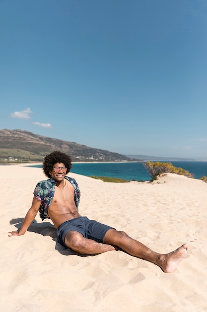 Giovane uomo atletico che si siede sulla spiaggia sabbiosa