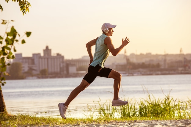 A young athletic man working out listening to the music at the riverside outdoors