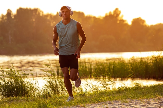 Free photo a young athletic man working out listening to the music at the riverside outdoors