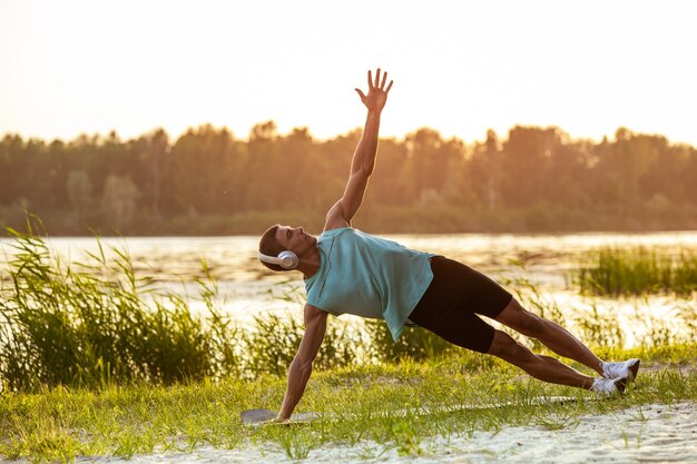 A young athletic man working out listening to the music at the riverside outdoors