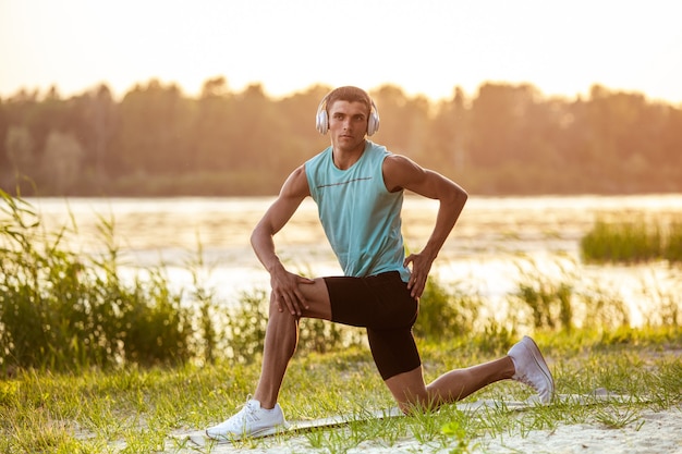 A young athletic man working out listening to the music at the riverside outdoors