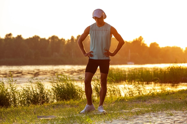 A young athletic man working out listening to the music at the riverside outdoors