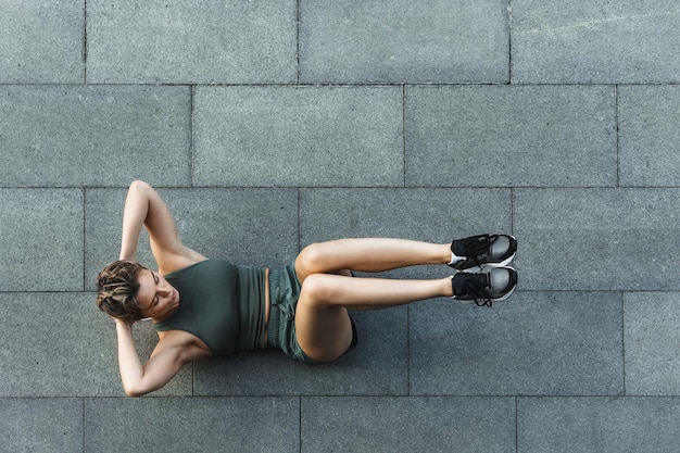 彼女​の​ストリートワークアウト中​に​コンクリート​の​床​で​腹部​の​クランチ​運動​を​している​若い​運動​選手