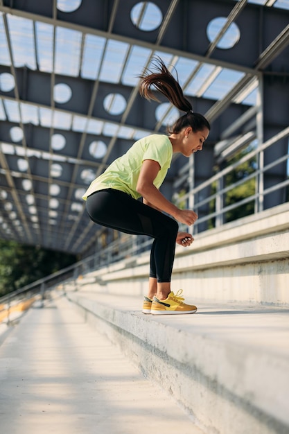 スクワットをしている若い運動の女性は、ステップにジャンプします