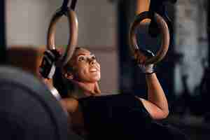 Free photo young athletic woman exercising strength on gymnastic rings during cross training in fitness center