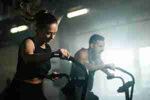 Free photo young athletic woman having cross training on stationary bike in a gym