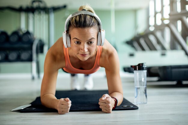 Young athletic woman in plank pose exercising strength at health club