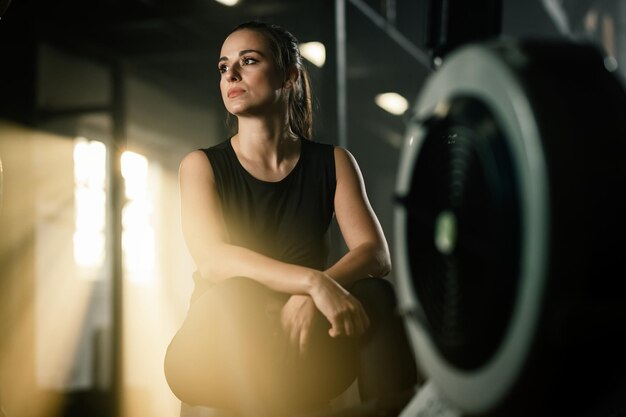 Giovane donna atletica che riposa dopo l'esercizio sul vogatore in una palestra