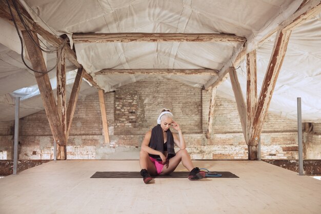 A young athletic woman in white headphones working out listening to the music on an abandoned construction site