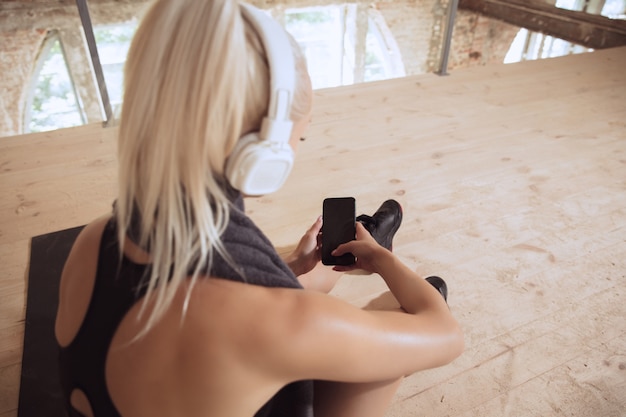 Free photo a young athletic woman in white headphones working out listening to the music on an abandoned construction site