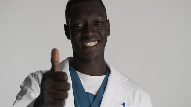 Молодой привлекательный афроамериканец-врач, указывающий на вас жестом на камеру, выглядит счастливым на белом фоне