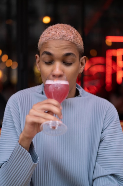 Giovane uomo afroamericano attraente nella caffetteria con cocktail cosmopolita rosa, servizio fotografico di moda. parigi