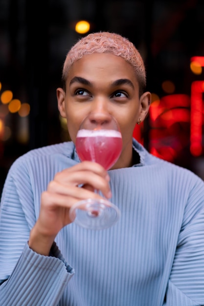 Giovane uomo afroamericano attraente nella caffetteria con cocktail cosmopolita rosa, servizio fotografico di moda. parigi