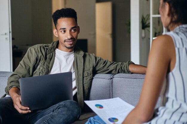 Young attractive African American man with laptop working with colleague in modern co-working space