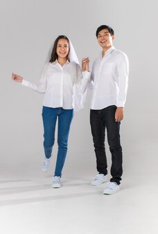 흰 셔츠와 베일을 끼고 걷고 웃고 있는 손을 잡고 있는 젊은 매력적인 아시아 부부