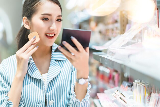 若い魅力的なアジアの女性陽気なショッピングモールで化粧品を選ぶことを楽しむボケ味の背景をぼかす