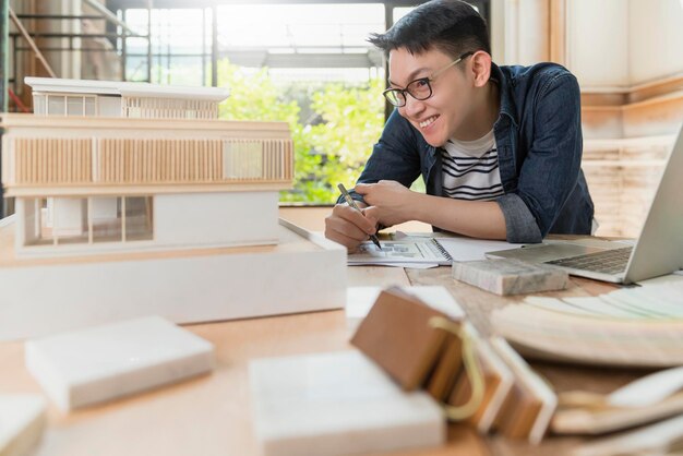젊은 매력적인 아시아 안경 남성 건축가는 집 디자인 프로젝트의 대량 모델 연구와 함께 새로운 프로젝트 하우스 모델 행복 아시아를 제시하는 것을 자랑스럽게 생각합니다.