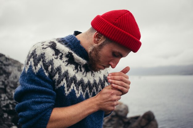 Young attractive bearded millennial man in red fisherman or sailor beanie hat and traditional icelandic ornament blue sweater