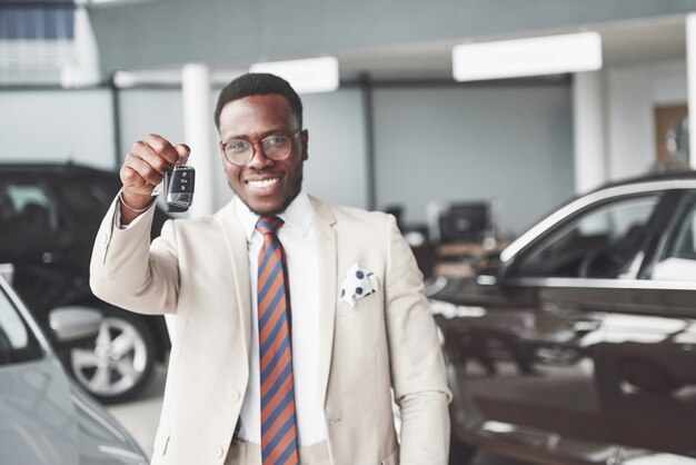 Молодой привлекательный темнокожий бизнесмен покупает новую машину, ключи он держит в руке. Мечты сбываются