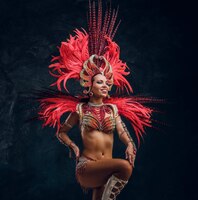 young attractive brasil dancer in red feather costume is dancing at small dark studio.