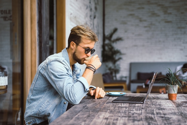 young attractive business man in a cafe works for a laptop, drinks coffee.