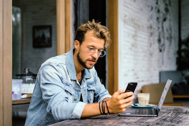 Free photo young attractive business man in a cafe works for a laptop, drinks coffee.